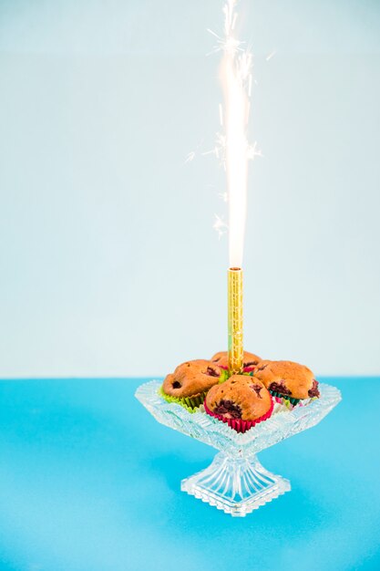 Un feu d'artifice scintille au milieu d'un cupcake sur un cakestand transparent sur fond rose