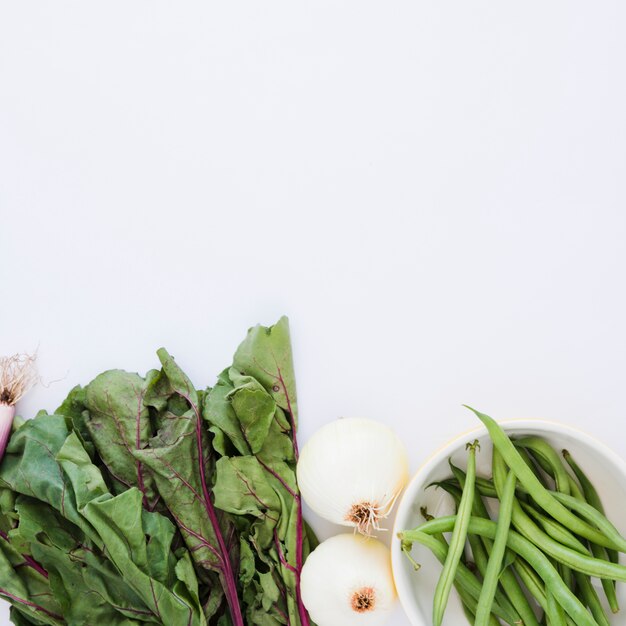 Feuilles de betterave rouge; oignons et haricots verts dans le bol sur fond blanc