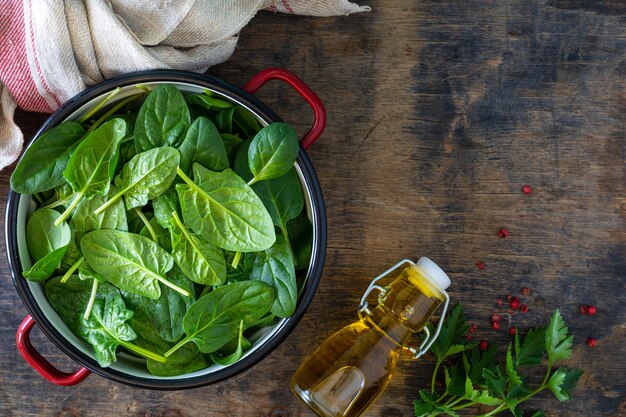 Des feuilles d'épinards fraîches dans un bol et de l'huile d'olive sur une table en bois