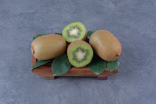 Feuilles et kiwi sur plaque de bois sur table en marbre.