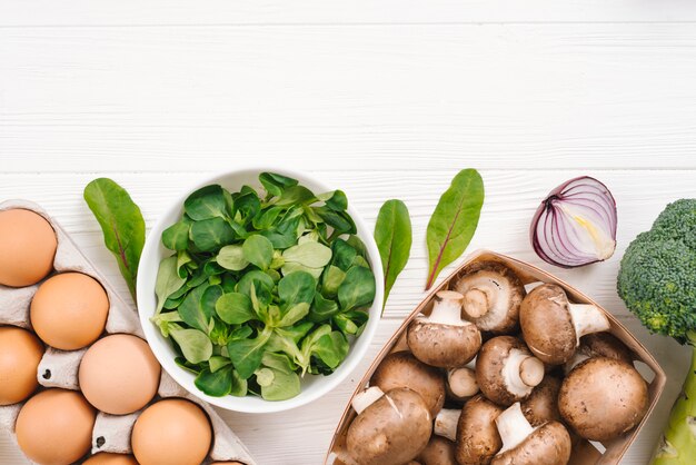 Feuilles de salade de maïs frais; des œufs; oignon; Brocoli et champignons sur un bureau blanc