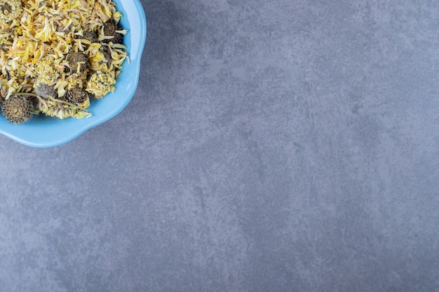 Feuilles de thé de variété dans un bol bleu sur fond gris.