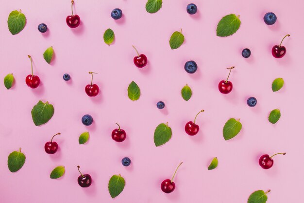 Feuilles vertes, cerises et myrtilles sur la surface rose