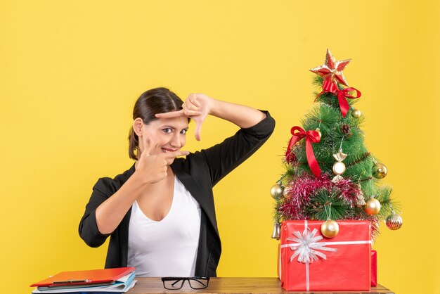 Fière jeune femme en costume avec arbre de Noël décoré au bureau sur jaune