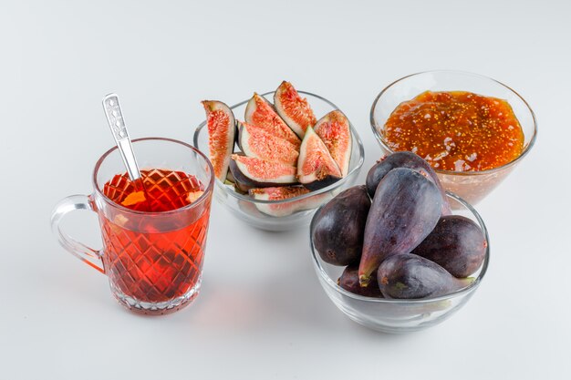 Figues avec confiture de figues, tasse de thé, cuillère à café dans des bols sur blanc, high angle view.