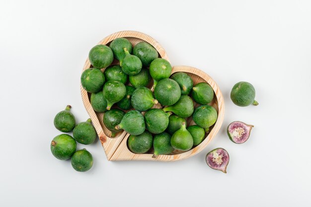 Figues dans une assiette en bois avec des tranches vue de dessus sur un mur blanc