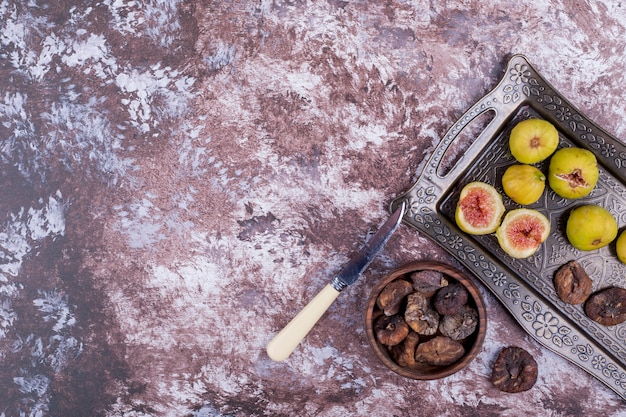 Figues entières, sèches et tranchées dans un plateau métallique et dans une tasse en bois.