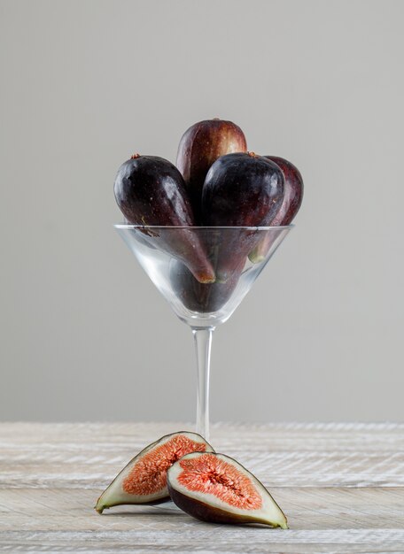 Figues de mission dans un verre à martini avec des moitiés de figues vue latérale sur une table en bois et fond gris