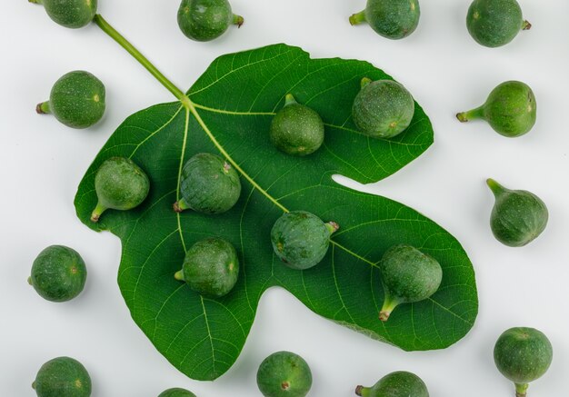 Figues mûres avec des feuilles sur un mur blanc, à plat.