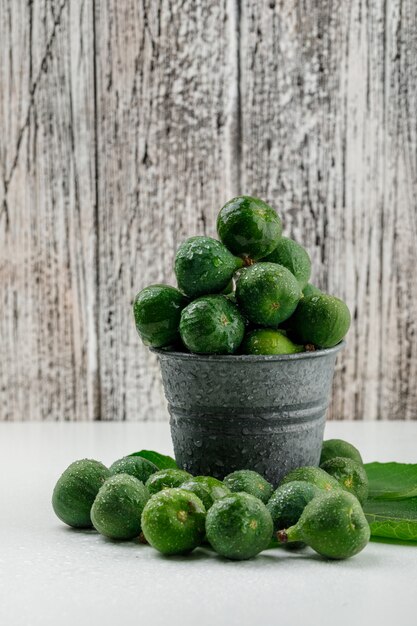 Figues des pluies avec des feuilles dans un mini seau sur mur en bois blanc et grungy, vue latérale.