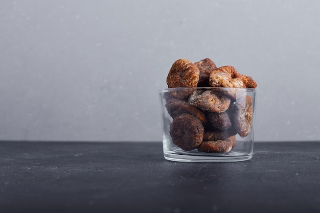 Figues séchées dans une tasse en verre sur fond gris.