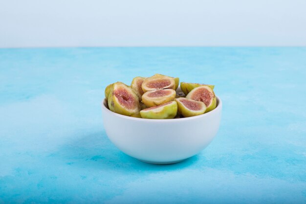 Figues vertes aux graines rouges dans un bol en céramique blanche sur bleu.