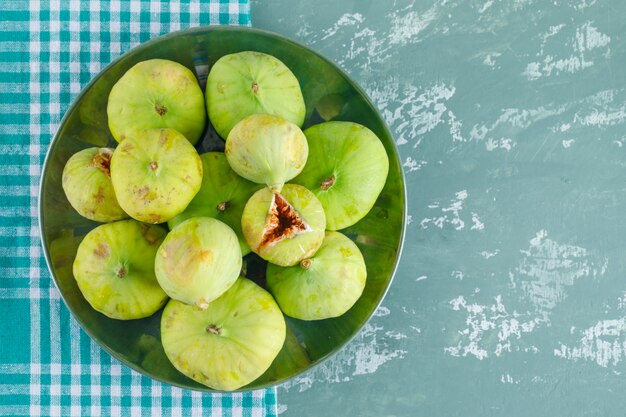 Figues vertes dans une assiette sur plâtre et toile de pique-nique. pose à plat.