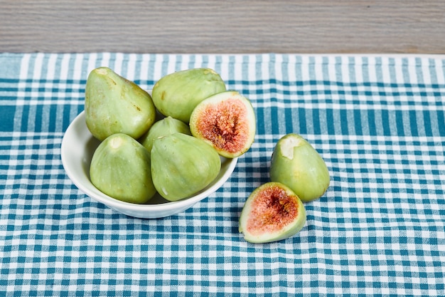 Figues vertes dans un bol blanc et sur une table en bois avec nappe bleue. Photo de haute qualité