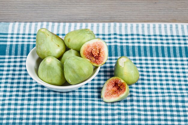 Figues vertes dans un bol blanc et sur une table en bois avec nappe bleue. Photo de haute qualité