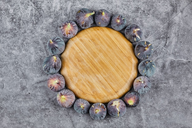 Photo gratuite figues violettes autour d'une assiette en bois sur marbre.