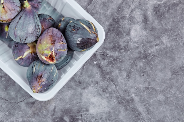 Figues violettes dans un récipient en plastique blanc.