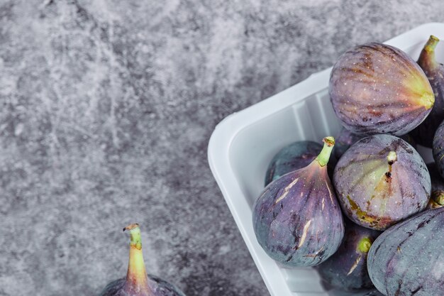 Figues violettes dans un récipient en plastique blanc.