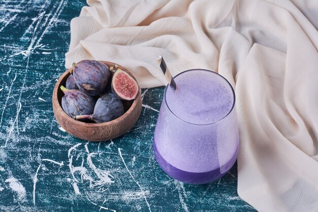 Figues violettes avec une tasse de boisson sur bleu.