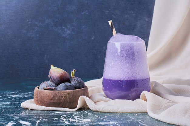 Figues violettes avec une tasse de boisson sur bleu.