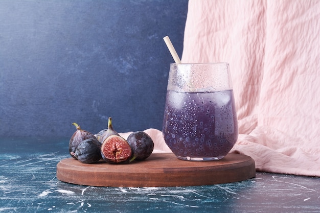 Figues violettes avec un verre de jus sur bleu.