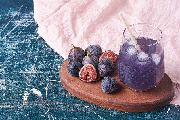 Figues violettes avec un verre de jus sur bleu.