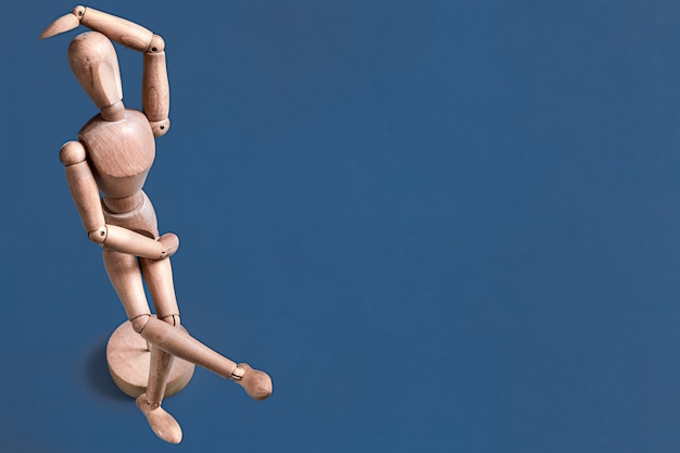 La figurine d'homme en bois sur un mur bleu.