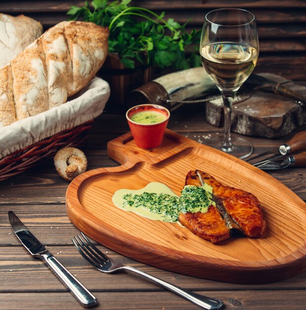 Filet de poisson grillé et servi avec une sauce crémeuse aux herbes et un verre de vin blanc.