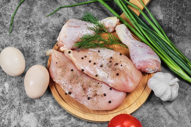 Filet de poulet cru et cuisses sur plaque en bois avec des légumes frais.