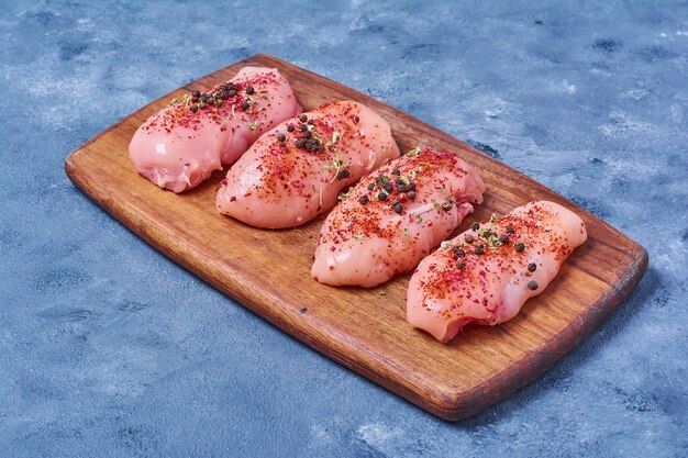 Filet de poulet cru sur une planche de bois sur bleu