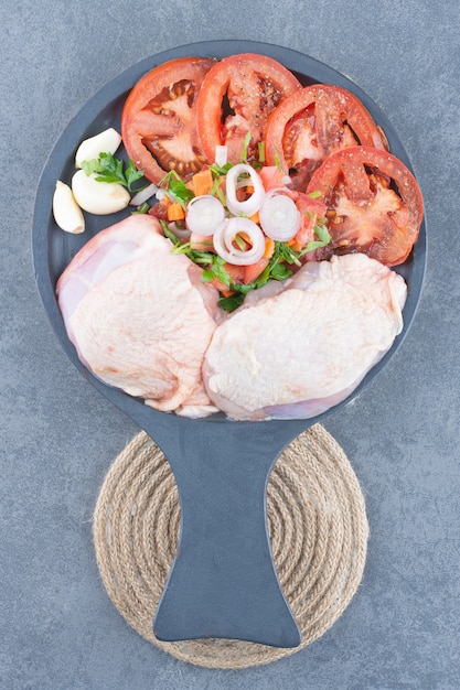 Filet de poulet non cuit avec des tranches de tomates sur une planche noire.