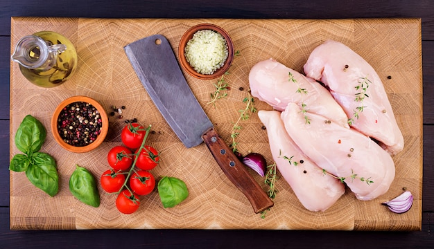 Filets de poitrine de poulet crus sur une planche à découper en bois avec des herbes et des épices. Vue de dessus