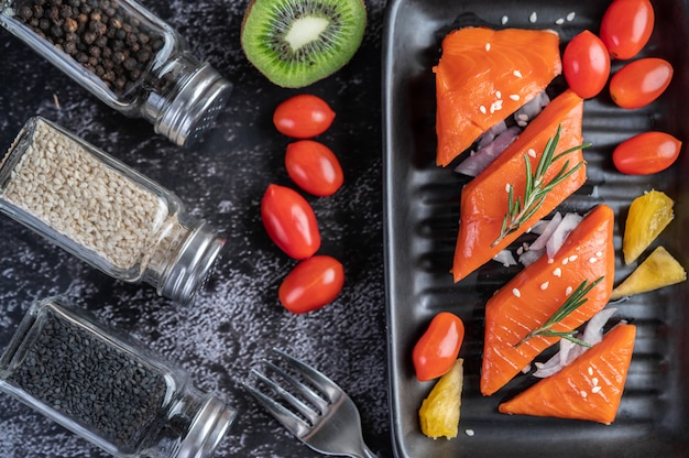 Photo gratuite filets de saumon cru, poivre, kiwi, ananas et romarin sur une plaque et un sol en ciment noir.
