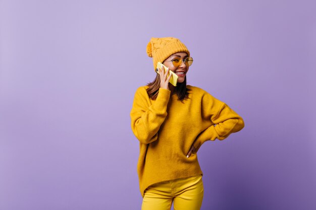 La fille adore la couleur orange et pose pour un nouveau portrait dans une tenue élégante. Modèle parlant au téléphone jaune, souriant sympathique