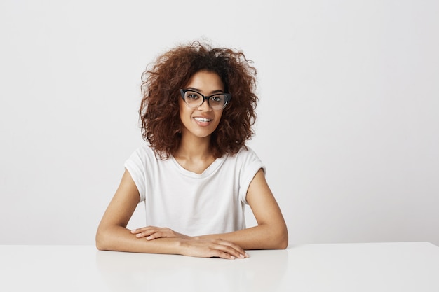 Fille africaine dans des verres, assis sur un mur blanc. Copiez l'espace.