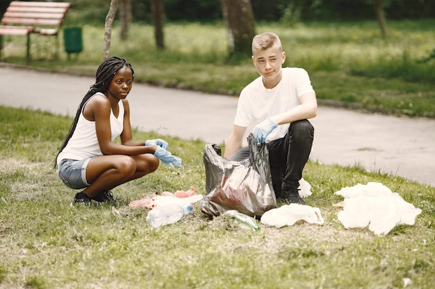 Fille africaine et garçon européen ramassant des ordures. Des militants nettoient le parc sur le côté.