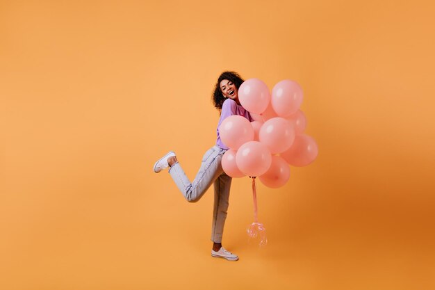 Fille africaine sensuelle posant avec des ballons à l'hélium rose Photo intérieure d'une merveilleuse femme brune dansant lors d'un événement