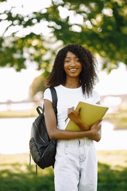 Fille africaine tenant un livre pour étudier en se tenant debout à l'extérieur. La fille regarde directement la caméra