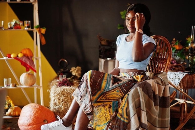 Photo gratuite fille afro-américaine assise sur une chaise berçante contre la décoration d'ambiance d'automne automne en afrique