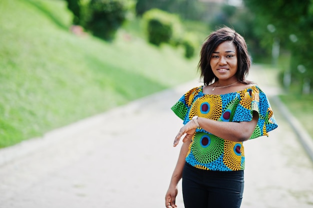 Fille afro-américaine en chemise colorée et pantalon noir posé en plein air