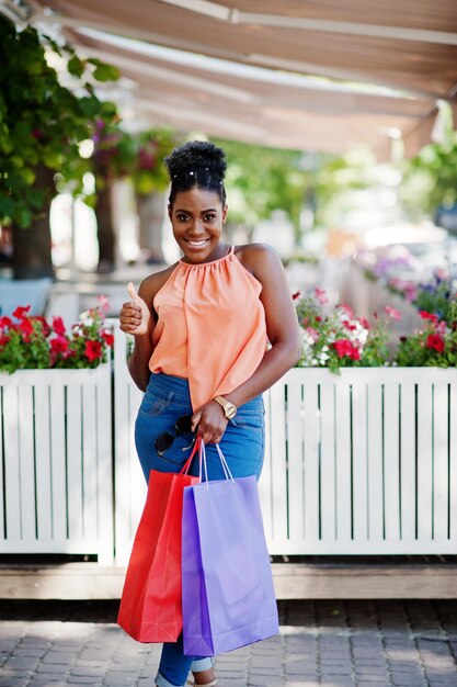 Fille afro-américaine décontractée avec des sacs à provisions colorés marchant en plein air