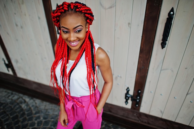 Fille afro-américaine à la mode au pantalon rose et dreads rouges posées en plein air