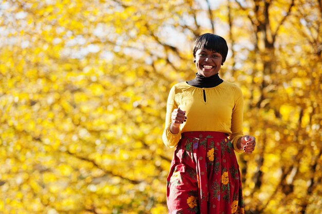 Fille afro-américaine en robe jaune et rouge au parc d'automne d'automne doré