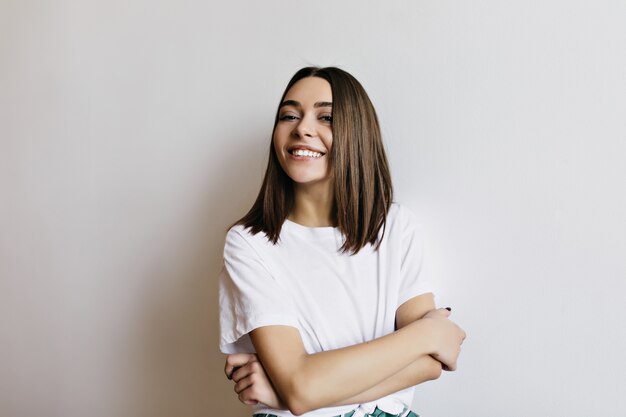 Fille agréable aux cheveux bruns brillants souriant. Photo intérieure d'une dame caucasienne debout, les bras croisés.