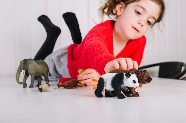 Fille allongée sur la table en jouant avec des jouets d&#39;animaux