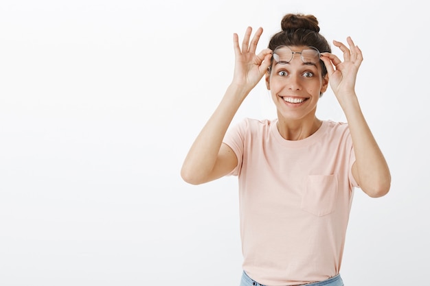 Fille amusée et surprise avec des lunettes posant contre le mur blanc