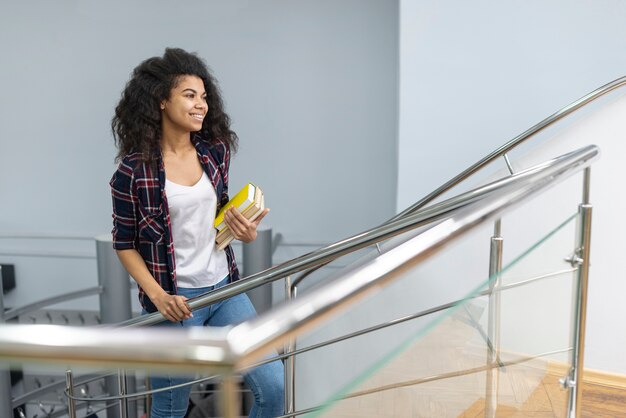 Fille d'angle élevé avec une pile de livres monter les escaliers