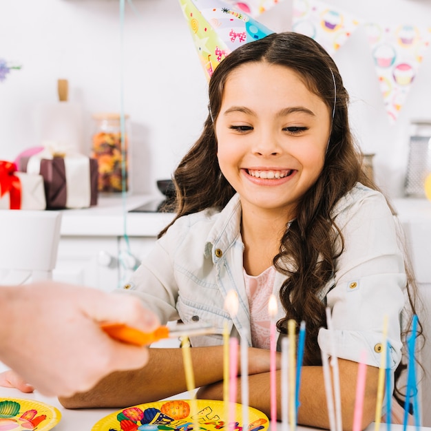 Fille d&#39;anniversaire souriante regardant la main d&#39;une personne allumant les bougies