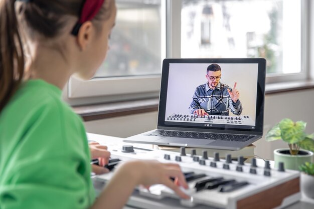 Une fille apprend à jouer du piano avec un professeur de musique d'apprentissage à distance en ligne