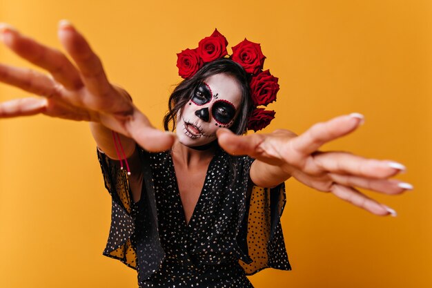 Fille avec l'art du visage beau mais effrayant tire les mains vers la caméra comme un zombie. Portrait de femme inhabituelle avec des roses rouges dans ses cheveux.